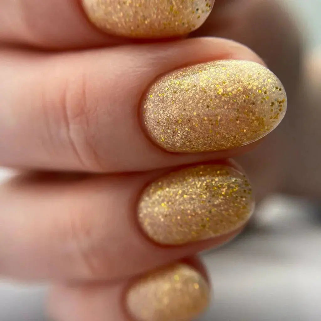 Hand holding gold glitter gel nails with three short oval tips