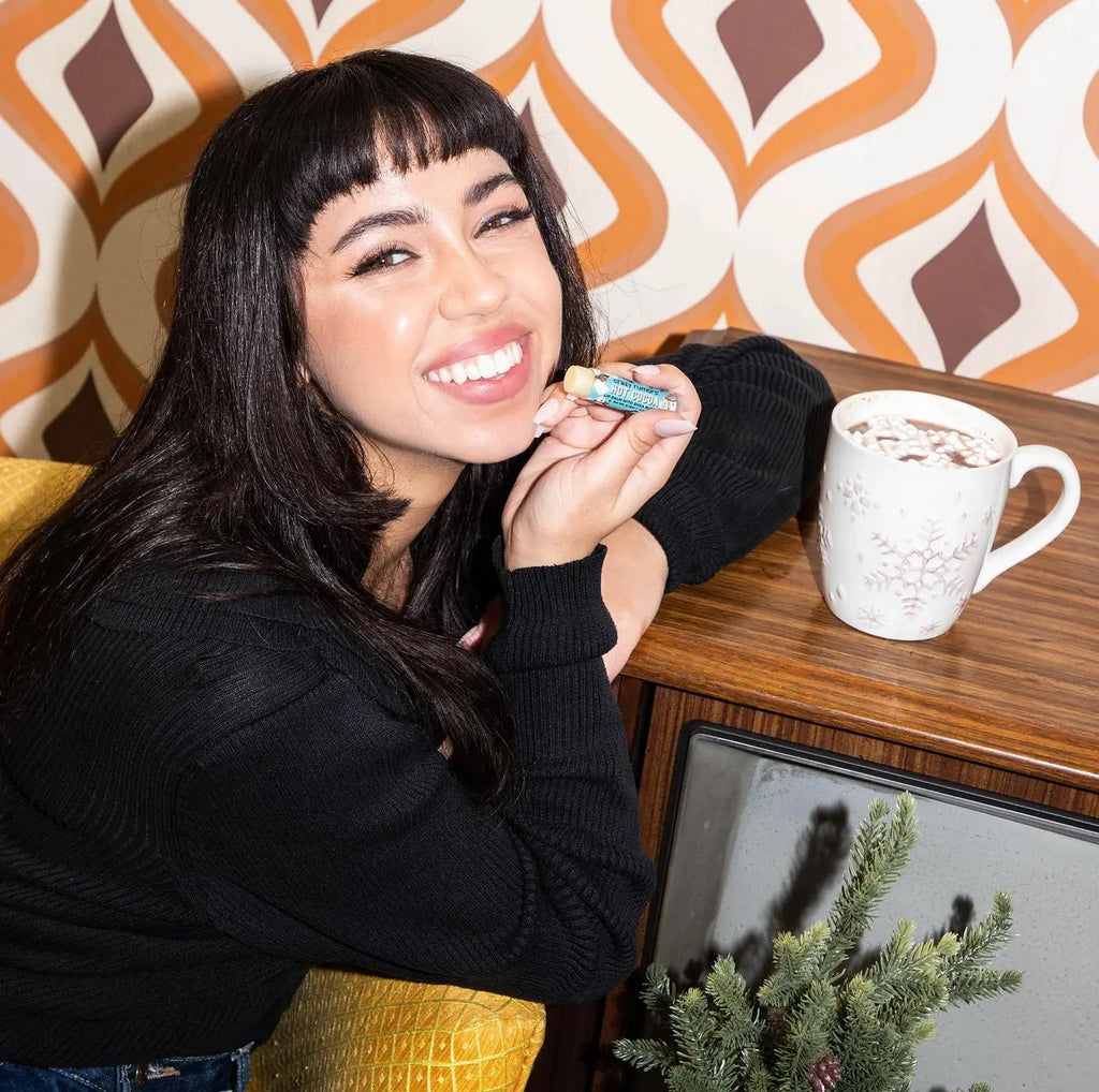 Person holding Hot Cocoa lip balm close to lips; blue-and-brown label on the tube
