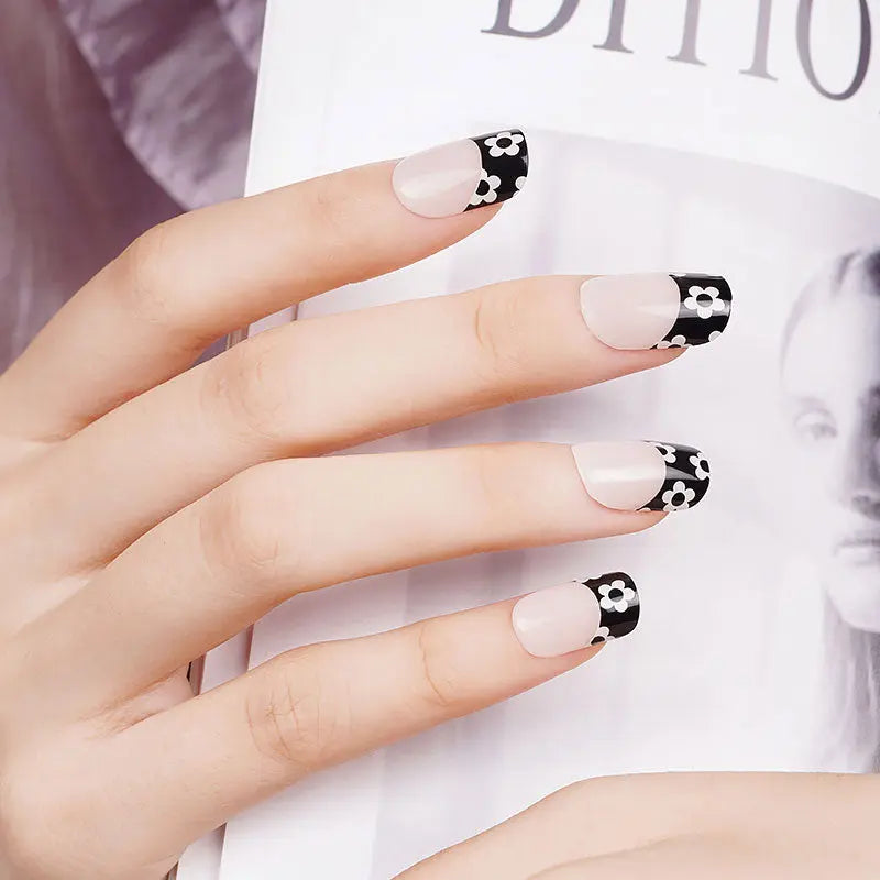 Gel Nail Strips auf Fingern: hellrosa Lack mit schwarzen Enden und weißen Blumen