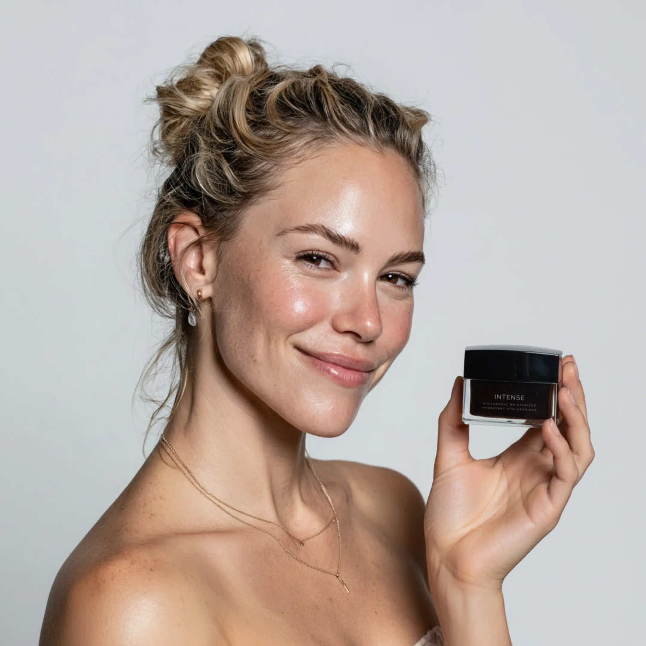 Hyaluronic moisturizer jar held near face, black lid and "INTENSE" label