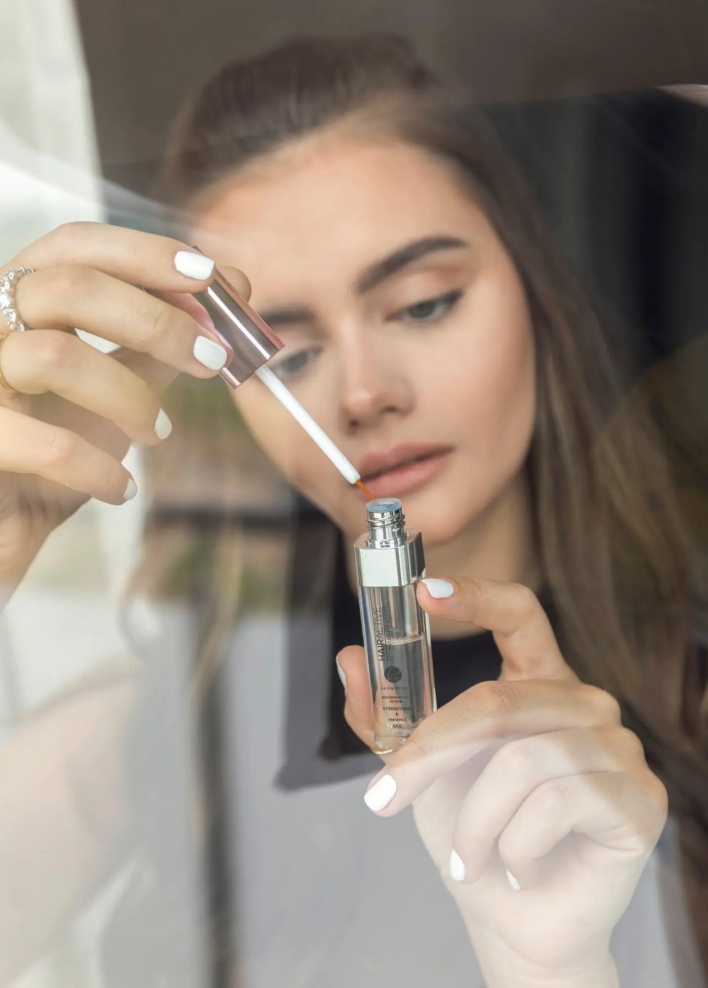 Eyebrow serum application close-up: wand brushing brows, bottle in hand