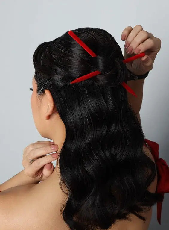 Two red velvet hairsticks securing a side bun in dark hair